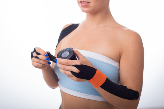 Female athlete puts a teip on her wrist. Kineziology, alternative treatment for injuries of joints and tendons. A woman is holding a roll of kineziotape. Lymphatic drainage. Close up.