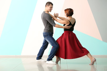 Cute loving couple dancing against color wall