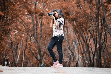 A Girl taking photo with camera in autumn colored background.