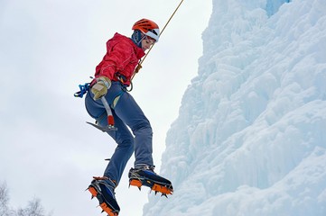 Fototapeta na wymiar Alpinist woman with ice tools axe in orange helmet climbing a large wall of ice. Outdoor Sports Portrait.