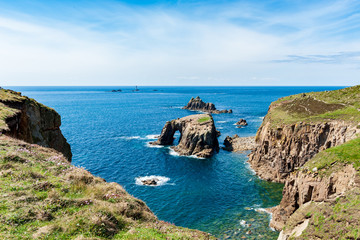 Fototapeta na wymiar Dry grassy cliffs overlooking Enys Dodnan Arch on a partially sunny day in Land’s End, UK.