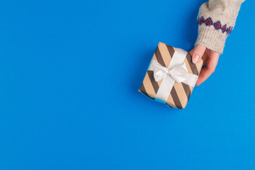 Small gift box in female hands on blue background, view from above