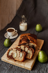 A seasonal cake with pears served on a wooden cutting board, fresh pears, coffee with milk in a white cup, milk in a bottle. Natural light. Vertical.