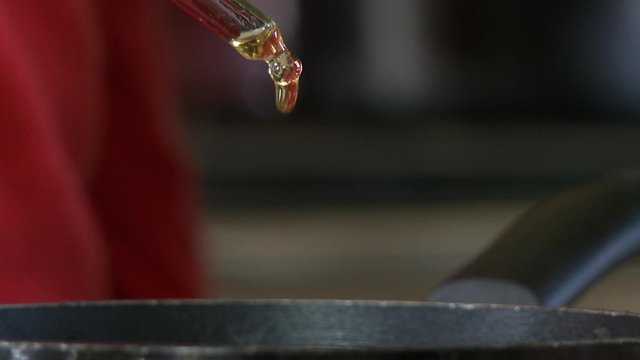 Handheld, close up shot of a dropper releasing drops of oil into a pot.