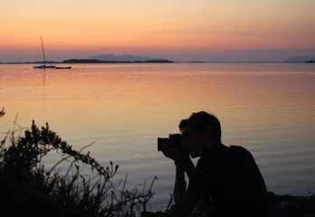 evocative imagine of young man taking a photo with his camera at sunset by the sea