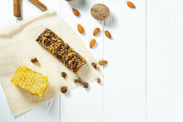 Close up on Granola Bar with honeycombs, nuts and cinnamon on craft paper on white wooden background. Healthy sweet dessert snack. Energy bar of muesli. Granola for breakfast. Copy space