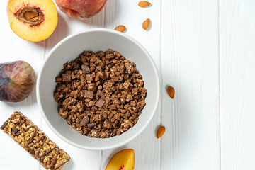 Top view on fresh chocolate granola in grey bowl with figs, peach on white wooden background. Copy space. Healthy and tasty breakfast. Vegan food. Food photo background