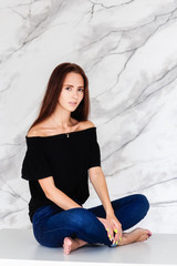 Young girl in jeans and black blouse is sitting on the table in the room