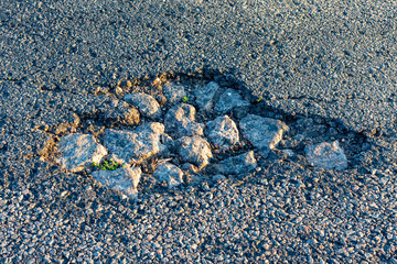 pothole on asphalt closeup with blue and gray stones. Background texture
