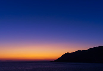 Fototapeta na wymiar Twilight vibrant colorful sky above sea and mountain sihlouette at dusk time.