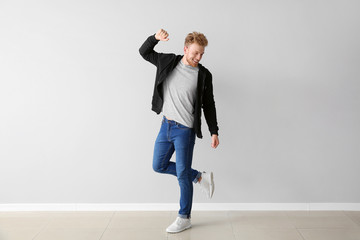 Handsome young man dancing against light wall