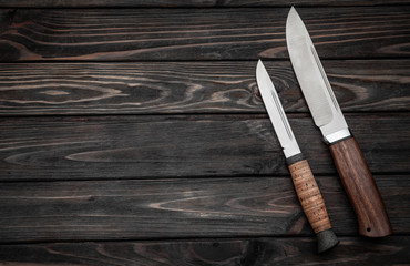 Hunting bowie knife with a wooden handle on dark wooden background. Steel arms weapon. top view