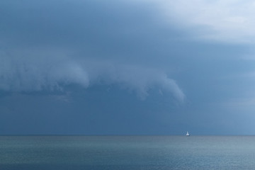 a small sailing boat drifts lost on the sea before a huge summer storm is coming