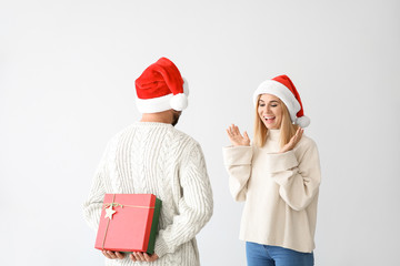 Man hiding Christmas gift for his wife behind back on light background