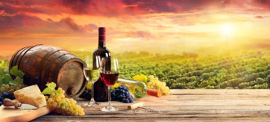 Barrel Wineglasses Cheese And Bottle In Vineyard At Sunset - obrazy, fototapety, plakaty