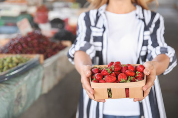 Woman with fresh strawberries in basket at market