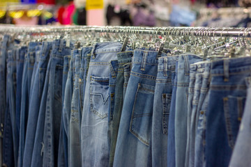 Many different blue Jeans on a hanging rack in the clothes shop store. Soft selective focus...