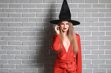 Beautiful woman dressed as witch for Halloween against brick wall