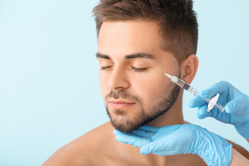 Handsome man receiving filler injection on color background