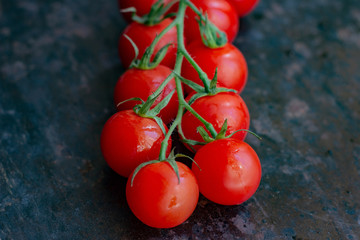 Fresh organic bright small red cherry tomatoes with green branch on dark brown and black rustic metal background