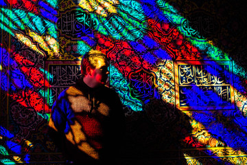 Obraz na płótnie Canvas Colours from the stained glass windows project on the wall and on a blonde european man leaning on the wall looking into the distance.