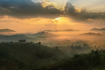 Mountain view misty morning of top hills around with sea of fog in valley and sun-rays in cloudy sky background, sunrise at Wat Kong Niam View Point, Khao Kho, Thailand.