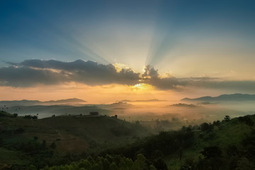 Mountain view misty morning of top hills around with sea of fog in valley and sun-rays in cloudy sky background, sunrise at Wat Kong Niam View Point, Khao Kho, Thailand.