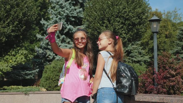 Schoolgirls rollerblading take a selfie on a smartphone. Best girlfriends teenagers being photographed in a summer park. Close-up 4k video