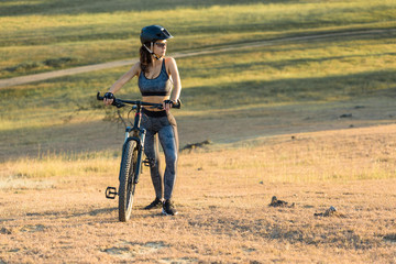 Girl on a mountain bike on offroad, beautiful portrait of a cyclist at sunset, Fitness girl rides a modern carbon fiber mountain bike in sportswear, a helmet, glasses and gloves.	