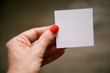 Fototapeta premium Female manicured hand is holding white empty square card. Soft focus. 