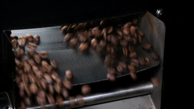 Close-up shot of roasted coffee beans spill out of a discharging flap cooler.