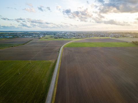 Aerial view of road surrounded by agricultural fields leading to small town in north of Lithuania - Joniskis