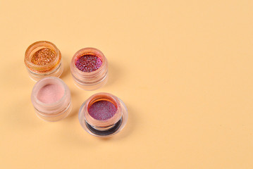 Cosmetics. Makeup. Jars with  crumbly bright shadows, glitter. Pink,peach, golden colors on beige background. Closeup. Space for text or design.