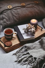 Cozy home with cup of tea with steam, blanket, book and candles. Hygge home interior