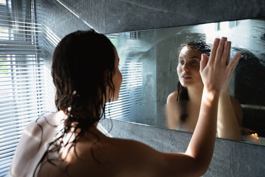 Young brunette woman in a modern bathroom wiping steam from a mirror