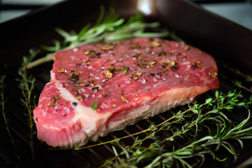 Raw steak with spices on grilling pan