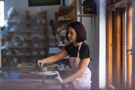 Female potter in a pottery studio forming pot on banding wheel