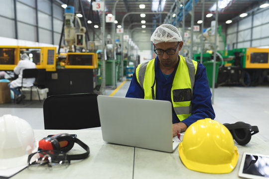 Male factory worker using laptop in a factory warehouse