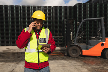 Forklift driver using smartphone and tablet outside factory warehouse