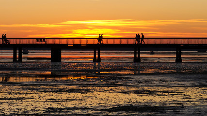 Fototapeta premium Silhouettes of people strolling on a jetty at sunset.