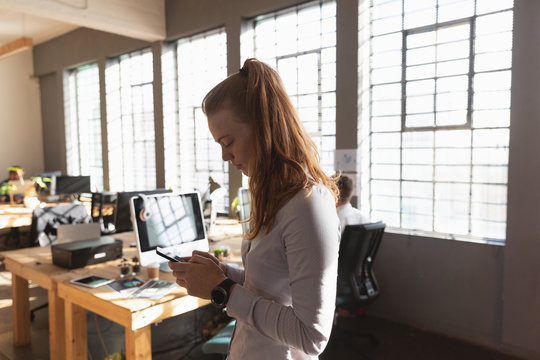 Young creative professional woman using smartphone  in a sunlit office