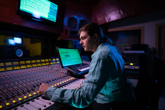 Male music producer working at the mixing desk in a sound studio 