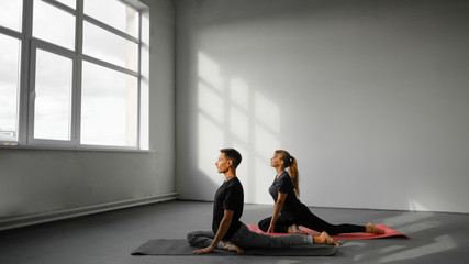 Young woman and man practicing yoga, doing Single Pigeon, Eka Pada Raja Kapotasana exercise, One Legged King Pigeon pose.