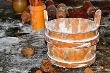 An old bucket of flour and pieces of gingerbread dough lying on the table. Rolling pins in the background