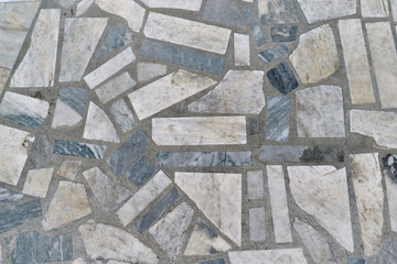 The surface is tiled with rectangular mosaic tiles of various sizes. The polygons are arranged in a chaotic order. Between tiles joints in concrete. Background, texture, background.