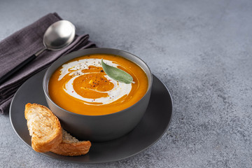 Pumpkin soup with cream on grey stone background. Copy space.