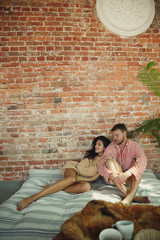 Fototapeta premium Couple of lovers at home relaxing together. Caucasian man and woman having weekend, looks tender and happy. Concept of relations, family, autumn and winter comfort. Lying together in sunlight.