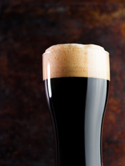 A glass of dark craft beer porter on a rusty brown dark background