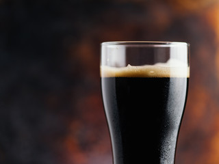 A glass of dark craft beer porter on a rusty brown dark background