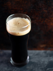 A glass of dark craft beer porter on a rusty brown dark background